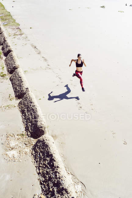 Mujer joven corriendo a lo largo de la playa - foto de stock