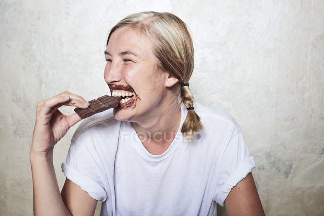 Donna che mangia barretta di cioccolato, cioccolato intorno alla bocca, ridendo — Foto stock