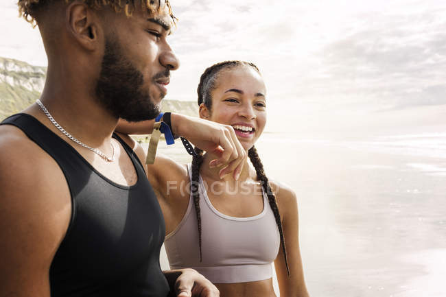 Jovens corredores femininos e masculinos descansando na praia — Fotografia de Stock