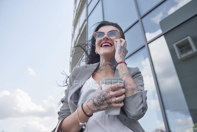 Femme d'affaires tenant du café et utilisant un smartphone — Photo de stock