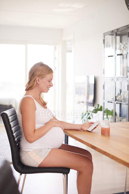 Side view of pregnant woman at desk looking at smartphone — Stock Photo