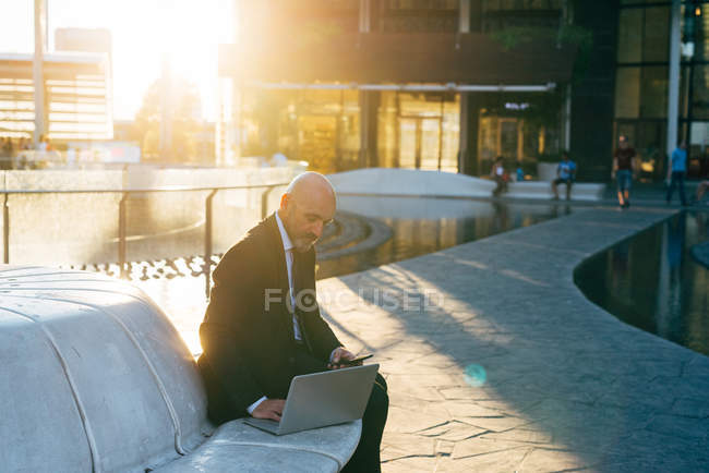 Reifer Geschäftsmann mit Laptop und Smartphone im Freien — Stockfoto
