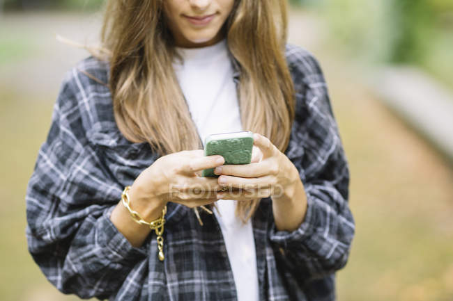 Captura recortada de mujer joven usando la pantalla táctil del teléfono inteligente en el parque - foto de stock