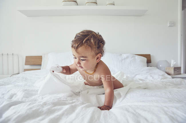 Criança sentada na cama, segurando papel higiênico desvendado — Fotografia de Stock