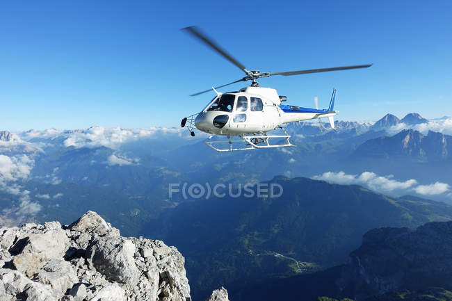 Helicopter approaching at mountain cliff edge — Stock Photo