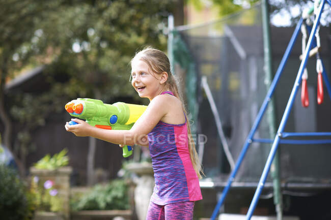 Девушка с мокрыми волосами держит водяной пистолет в саду — стоковое фото