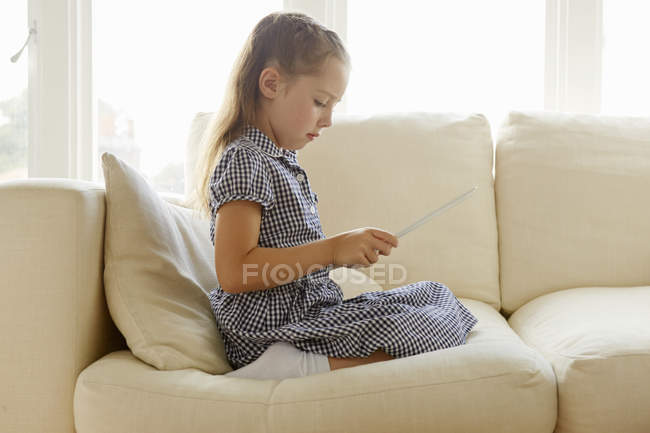 Молода дівчина сидить на дивані з цифровим планшетом — стокове фото