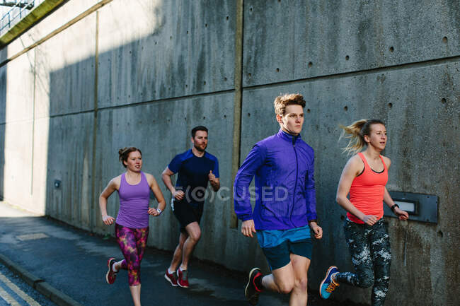 Чотири молоді дорослі бігуни біжать міським тротуаром — стокове фото