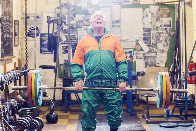 Старший пауэрлифтер изо всех сил пытается поднять штангу в спортзале — стоковое фото