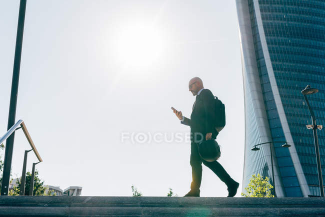 Uomo d'affari maturo che cammina all'aperto, portando il casco da moto, utilizzando lo smartphone — Foto stock
