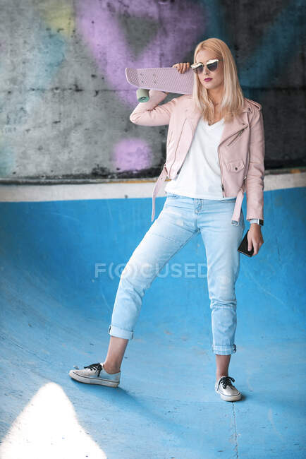 Portrait of young blond female skateboarder wearing sunglasses on skateboard ramp — Stock Photo