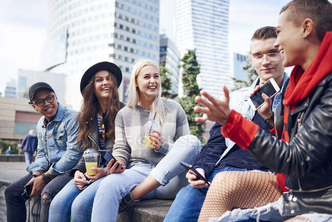 Five young adult friends sitting on wall chatting in city — Stock Photo
