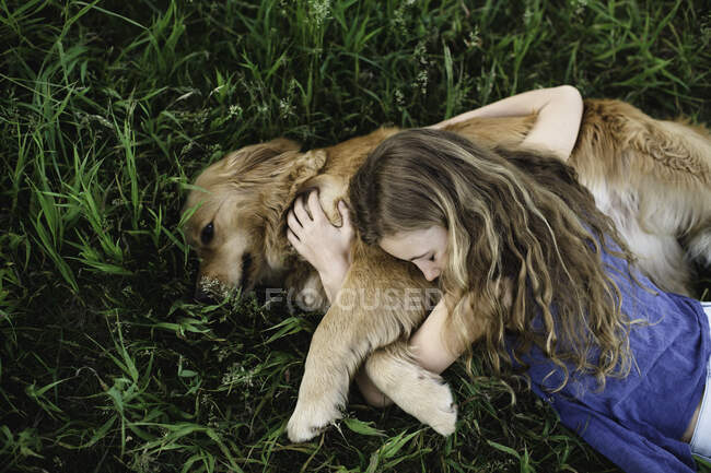 Overhead view of girl lying on grass hugging golden retriever dog — Stock Photo