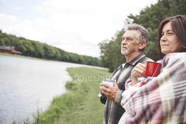Casal maduro em pé em ambiente rural com bebidas quentes — Fotografia de Stock