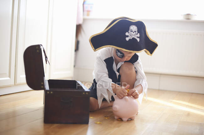 Chico joven vestido de pirata, poniendo dinero en alcancía - foto de stock
