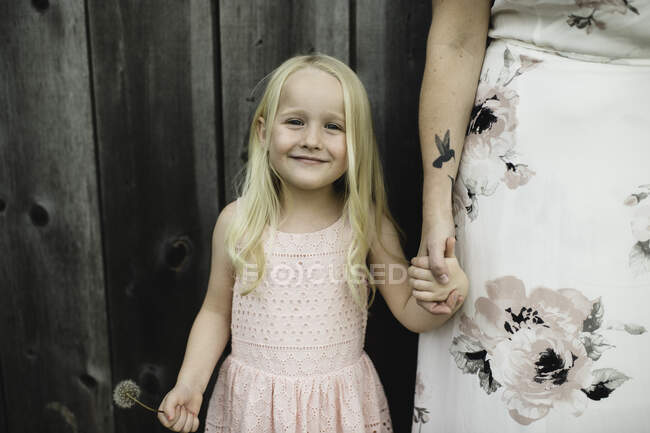 Retrato de niña sosteniendo el reloj de diente de león y la mano madre mirando a la cámara sonriendo - foto de stock