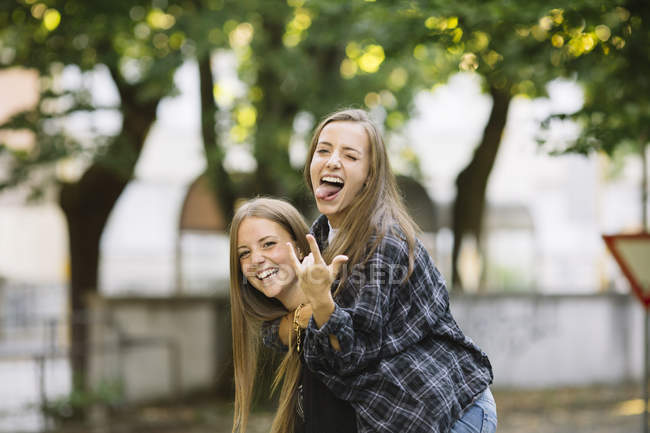 Portrait of young woman giving friend piggy back in park — Stock Photo
