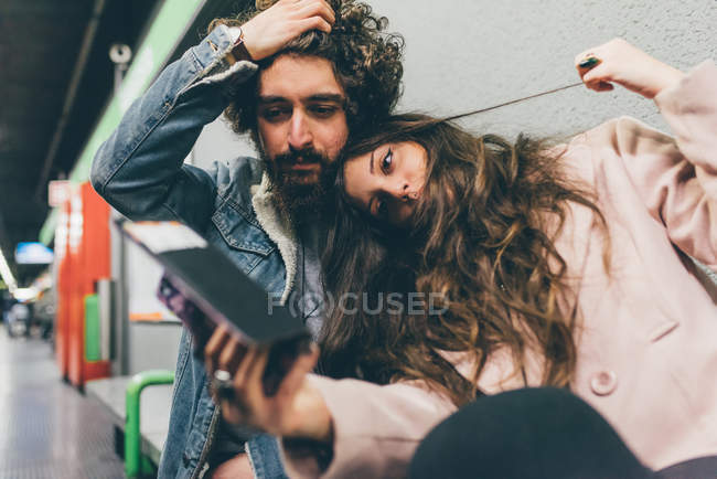 Young couple sitting in train station, looking at smartphone, worried expressions — Stock Photo