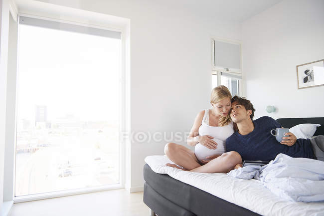 Romantic pregnant couple relaxing on bed — Stock Photo