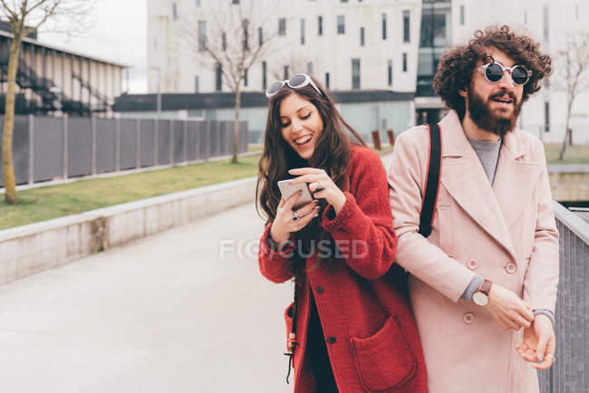 Jovem casal ao ar livre, jovem mulher olhando para o smartphone, rindo — Fotografia de Stock