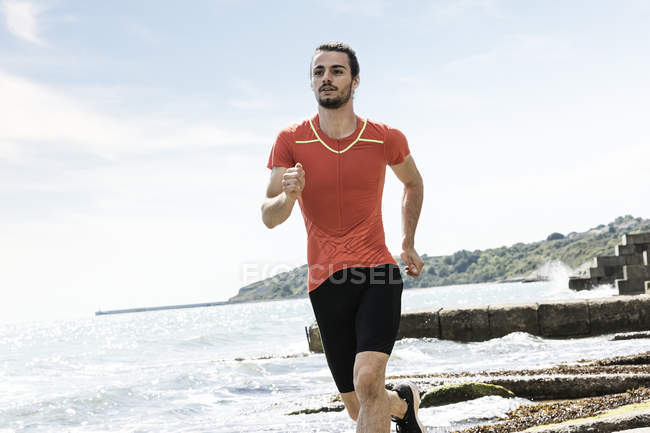 Giovane uomo che corre lungo la spiaggia — Foto stock