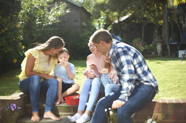 Familia, sentada en el jardín, comiendo dulces - foto de stock