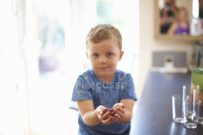 Portrait of boy holding handful of fresh grapes in kitchen — Stock Photo
