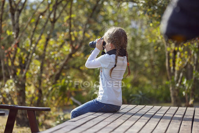 Дівчина в сільській місцевості, сидить на палубі, дивиться через бінокль — стокове фото