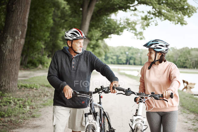 Älteres Ehepaar läuft mit Fahrrädern auf Landweg — Stockfoto
