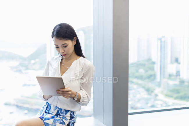 Mujer sentada en el alféizar de la ventana usando tableta digital - foto de stock