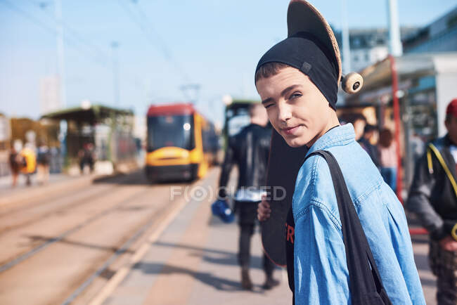 Retrato de la joven patinadora fresca en gorro sombrero en la estación de tranvía - foto de stock