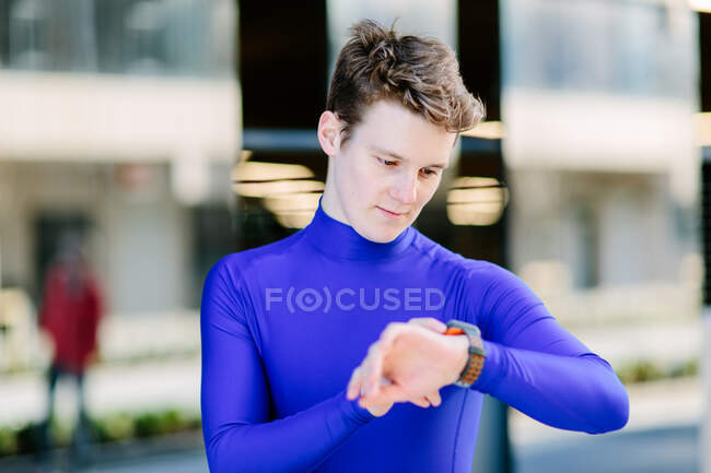 Junger männlicher Läufer blickt auf Smartwatch auf Bürgersteig in der Stadt — Stockfoto
