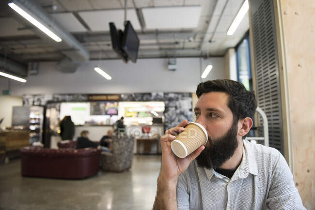 Мужчина пьет из одноразовой чашки в кафе — стоковое фото