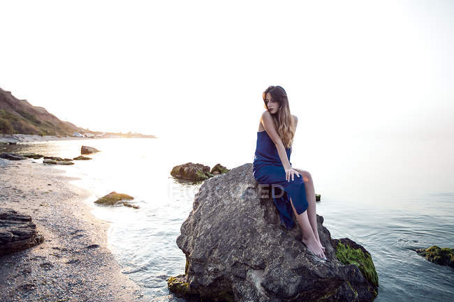 Молода жінка сидить на пляжному камені — стокове фото