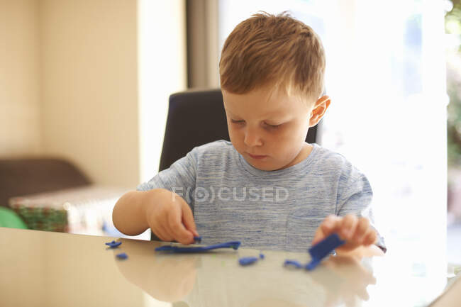 Junge sitzt am Tisch und spielt mit Modelliermasse — Stockfoto