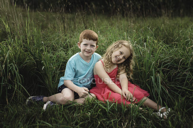 Portrait of girl and brother sitting in field — Stock Photo