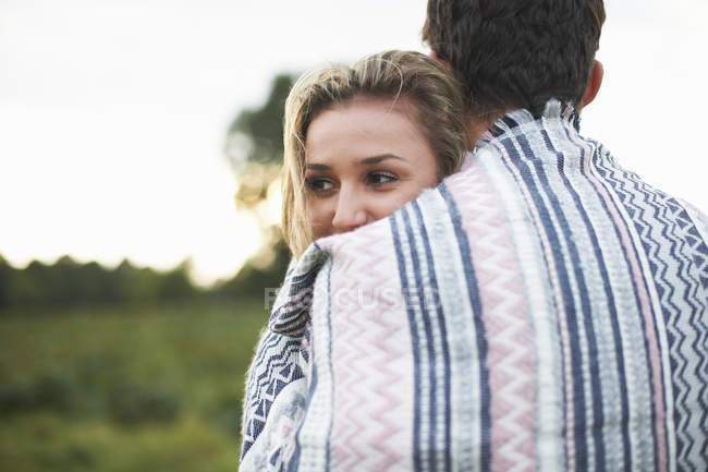 Young couple wrapped in blanket hugging in field — Stock Photo