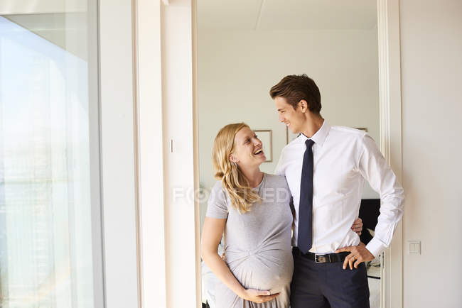 Вагітна пара посміхається один одному у вітальні — стокове фото