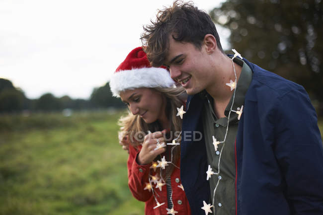 Young couple in santa hat and light garland in field — Stock Photo