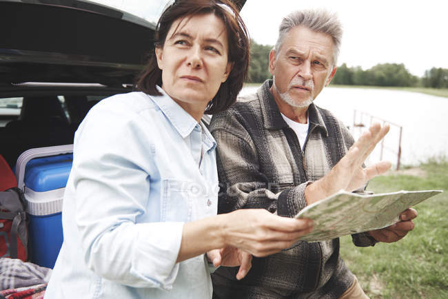 Couple d'âge mûr près de voiture avec carte en milieu rural — Photo de stock