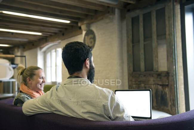 Колеги на дивані використовують ноутбук посміхаючись — стокове фото