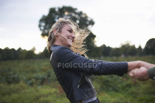 Jeune femme tenant des mains de petit ami et tournant autour dans le champ — Photo de stock