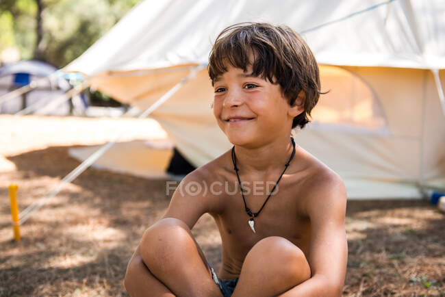 Niño pecho desnudo feliz sentado en el camping - foto de stock