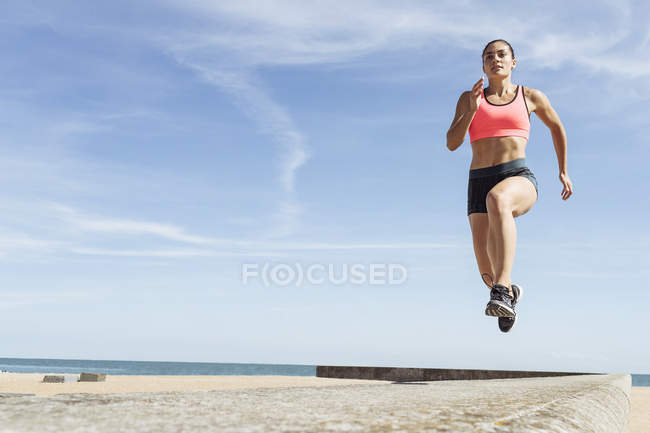 Mujer joven corriendo a lo largo del muro marino - foto de stock
