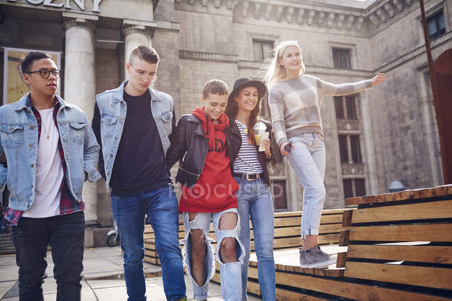 Cinco amigos adultos jóvenes caminando juntos en la ciudad - foto de stock