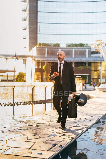 Uomo d'affari maturo che cammina con borsa e casco da moto — Foto stock