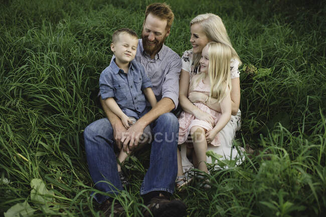 Family sitting in tall grass together smiling — Stock Photo