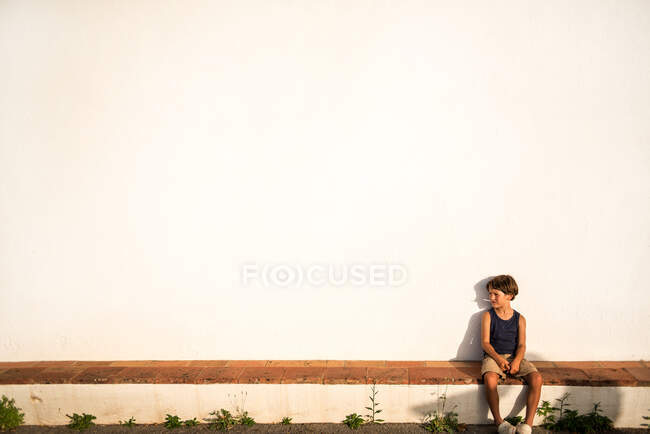 Мальчик сидит на стене возле белой церкви — стоковое фото