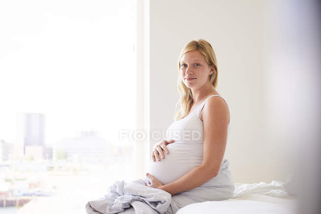 Portrait of pregnant young woman sitting on bed — Stock Photo
