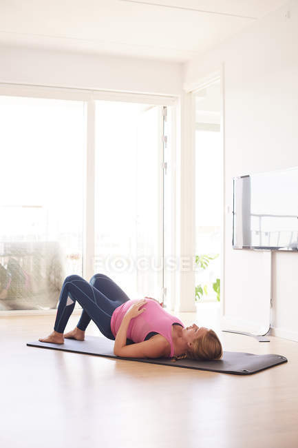 Вагітна молода жінка вправляється на йога килимок у вітальні — стокове фото